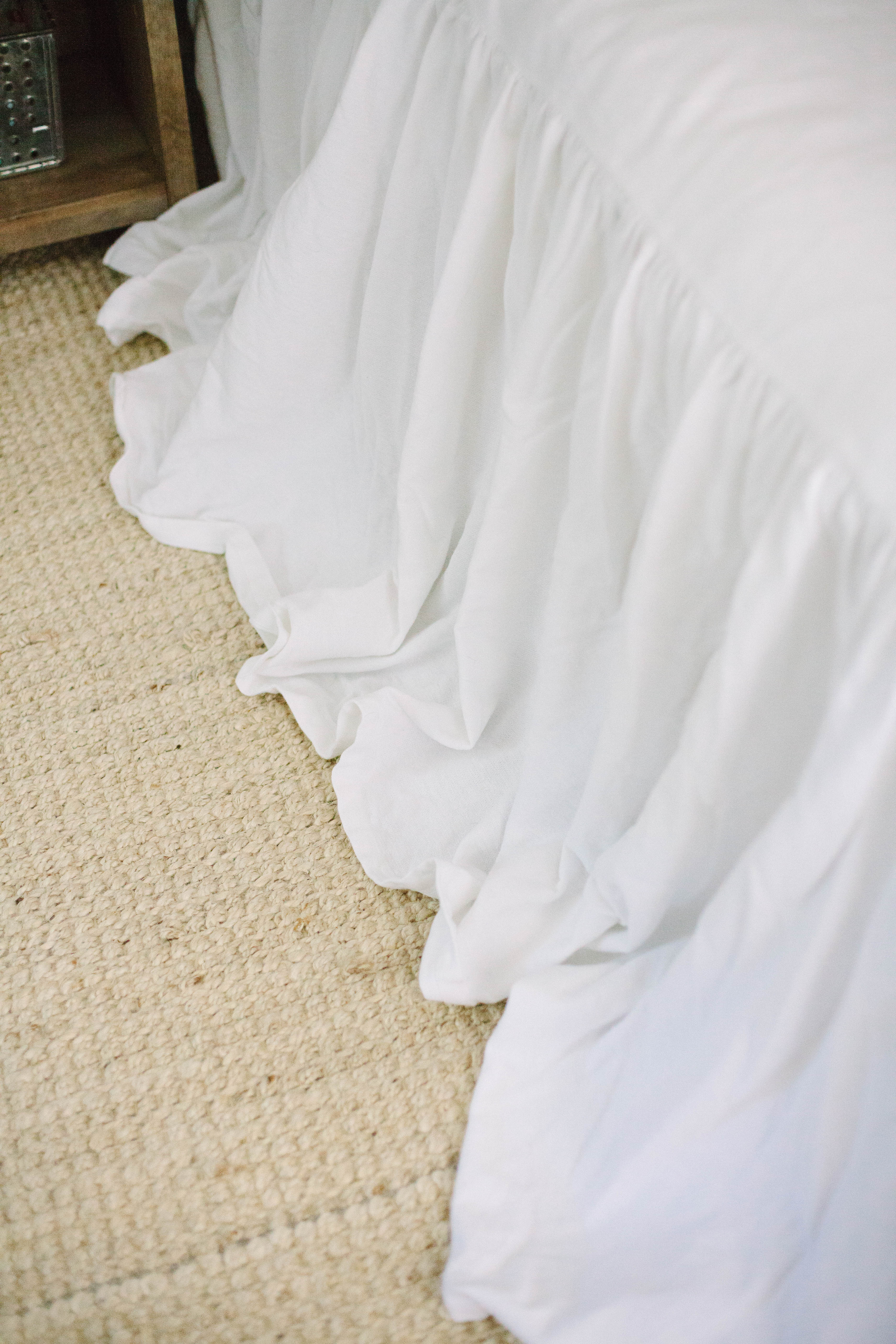 The summer cottage master bedroom is romantic with it's upholstered headboard and waterfall bedding, complete with a jute rug.